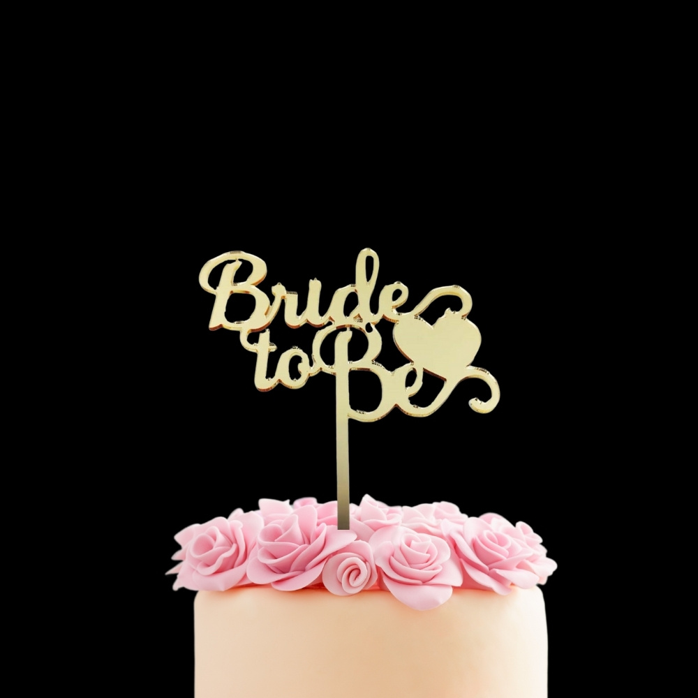 Altın renkli pleksi Bride To Be yazısı, pembe güllerle süslenmiş pastanın üzerinde